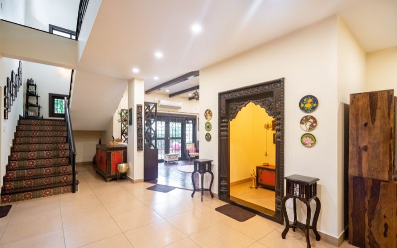 A traditional Kerala interior design style ornate doorway beside a staircase adorned with colorful, patterned tiles and decorative wall plates.