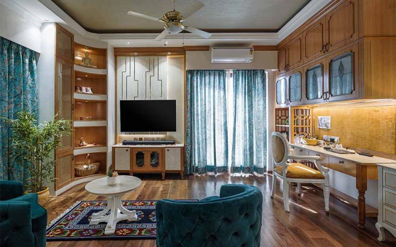 A stylish living room featuring a television, comfortable couches, and a desk, designed by the best interior designers in Kolkata.