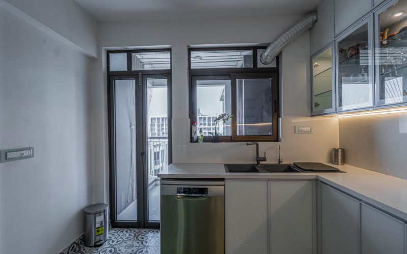 An elegant attractive kitchen interior showcasing a sink, window and sliding door with balcony, crafted by a Kolkata-based interior design firm.