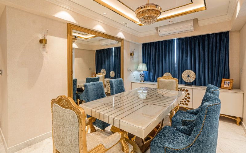 A stylish luxury dining room featuring blue chairs and a decorative mirror, showcasing classy luxurious home interior design in Kolkata.