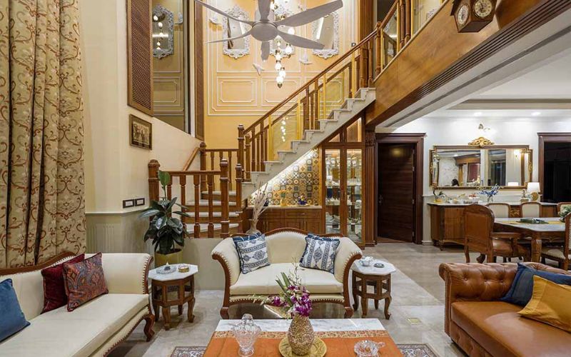 A beautifully designed living room with a staircase and a large chandelier, exemplifying the talent of Bangalore's interior designers.