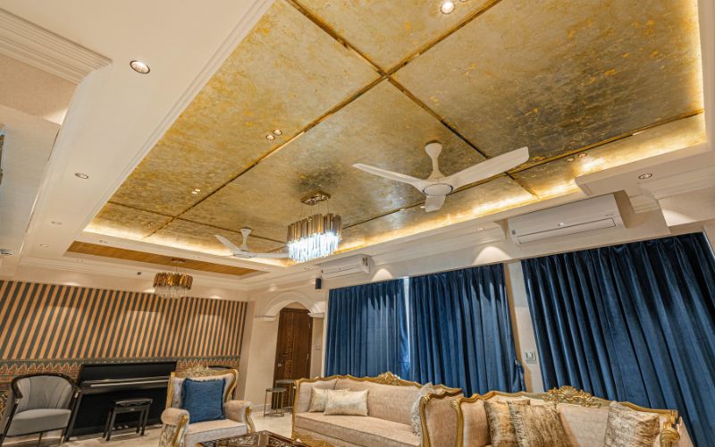 A luxurious living room featuring a gold ceiling and elegant blue curtains, designed by an interior designer in Kolkata.