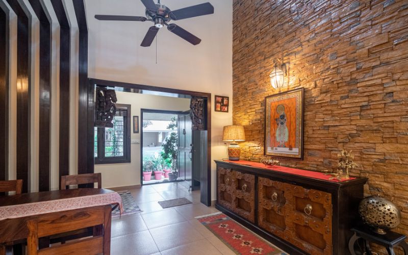 Cozy Kerala interior design corner with brick walls, wooden ceiling fan, artwork and stairs.