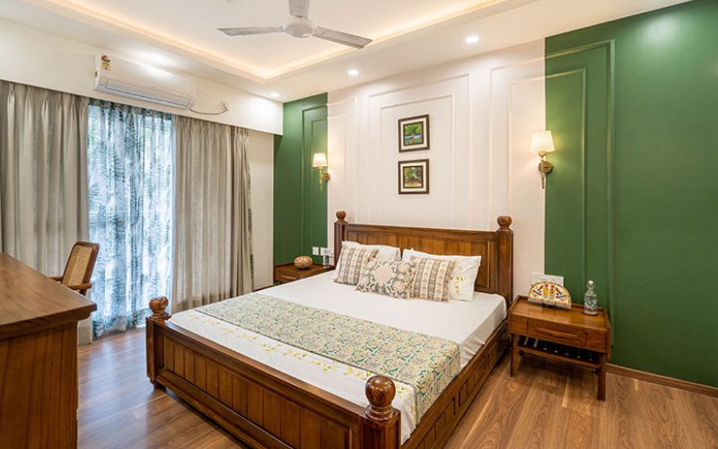 A stylish bedroom featuring green walls and wooden floors, designed by interior designers in Bangalore.