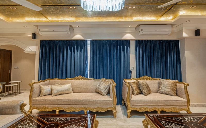 Opulent living room with gold furnishings and a chandelier, designed by a professional interior designer in Bangalore.