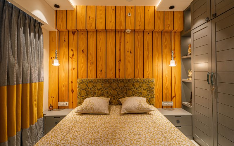 A cozy bedroom featuring yellow and white bedding against warm wooden walls designed by an interior designer in Kolkata.