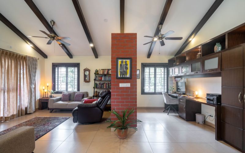 A stylish Kerala style living room featuring a brick wall design and a ceiling fan, designed by expert interior decorators for a cozy ambiance.